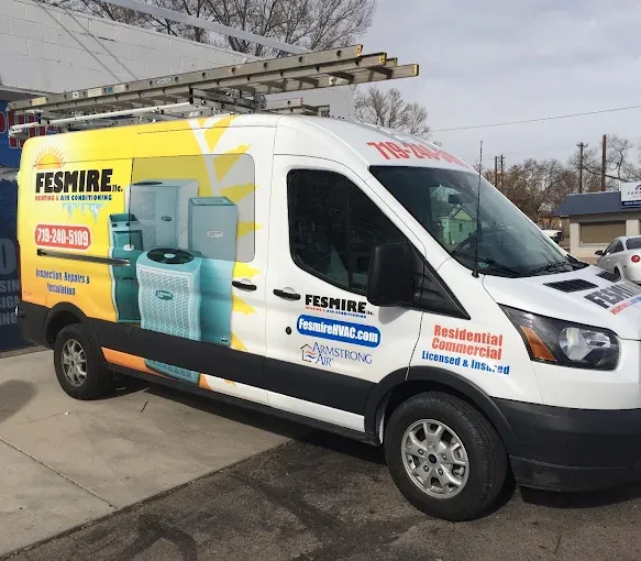 A Fesmire Heating & Air Conditioning service van, wrapped in the company’s sun logo and phone number, parked outside the shop