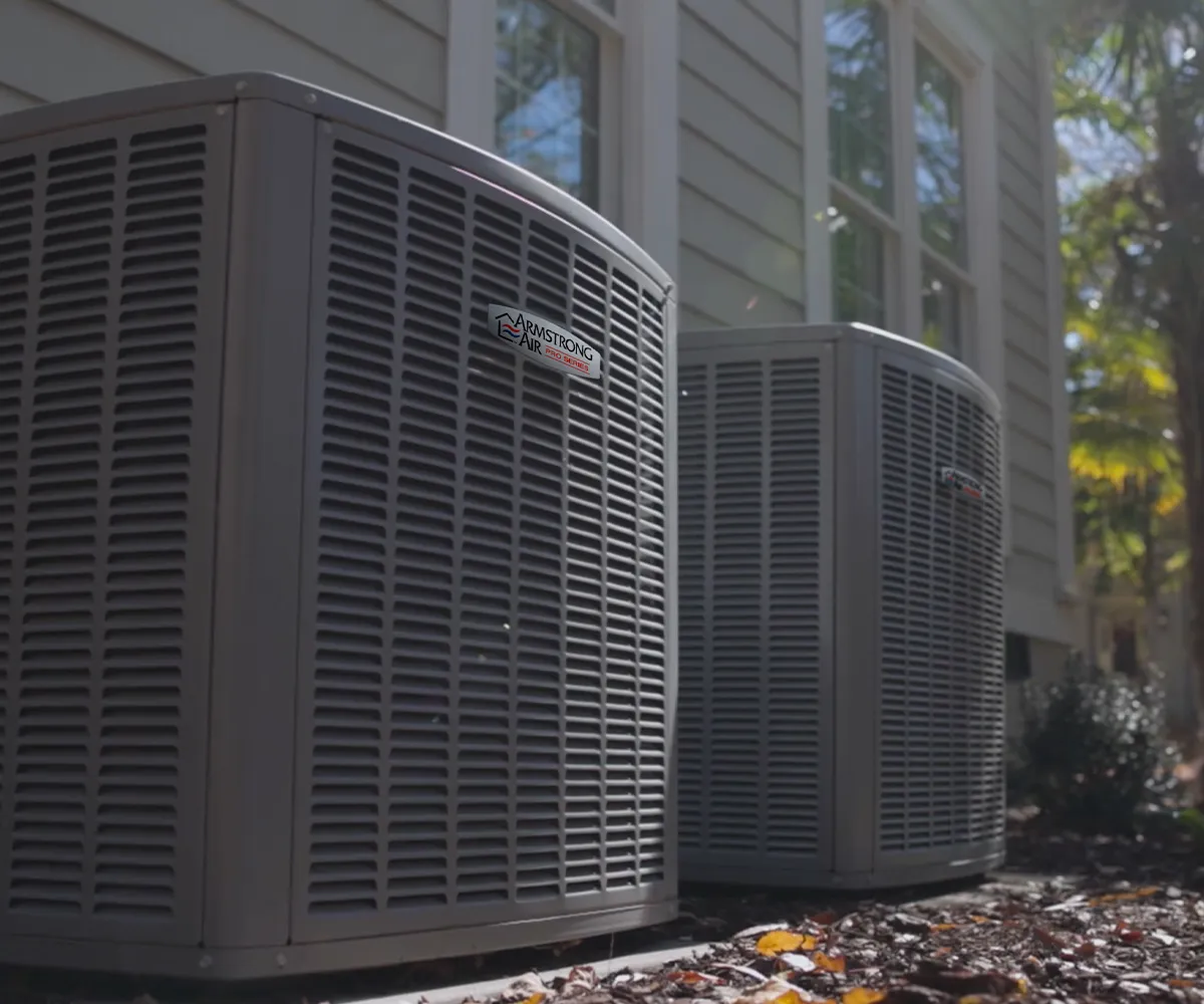 Two Armstrong Air outdoor units beside a gray-sided home